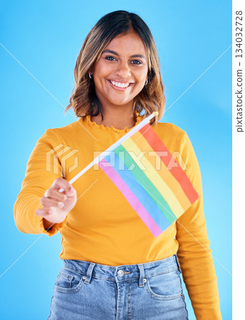 Portrait, flag and gay pride with a woman on a blue background in studio feeling proud of her lgbt status. Smile, freedom and equality with a happy young female holding a symbol of inclusion 134032728