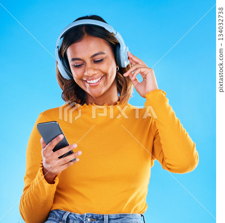 Happy woman, music headphones and phone in studio, blue background and happiness. Female model, smile and mobile for audio, streaming online radio and listening to podcast sound on media subscription Happy woman, music headphones and phone in studio, blue background and happiness. Female model, smile and mobile for audio, streaming online radio and listening to podcast sound on media subscription 134032738