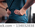 Hands, back and injury with a sports man holding a muscle in pain while training in a gym for health. Fitness, accident and anatomy with a male athlete suffering from an injured body during exercise 134032838