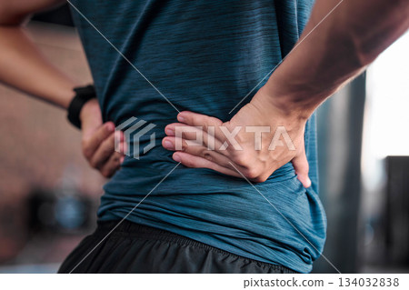 Hands, back and injury with a sports man holding a muscle in pain while training in a gym for health. Fitness, accident and anatomy with a male athlete suffering from an injured body during exercise 134032838