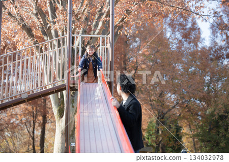 Parents and children playing on a slide in a park with autumn leaves 134032978