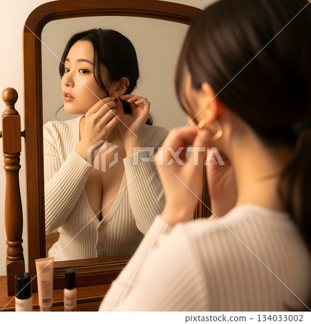 女人一邊照鏡子一邊戴耳環。 134033002