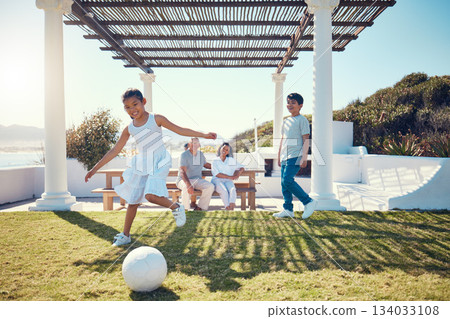Family, vacation and children playing soccer on a lawn in a holiday house and girl kick a ball having fun outdoors. Happy, excited and grandparents watch kids on the grass to play football 134033108
