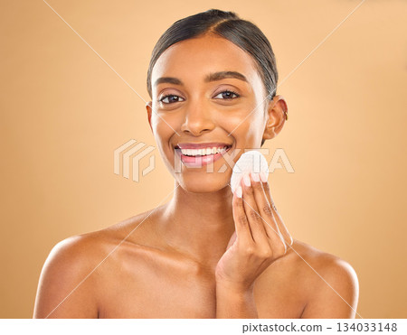 Skincare, happy and portrait of woman with cotton for facial cleansing isolated on a background. Smile, beauty and an Indian model cleaning her face with a pad for gentle treatment and makeup removal 134033148