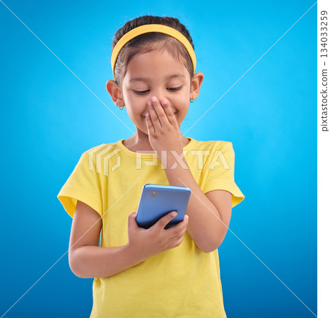 Phone, smile and child laugh on blue background for social media, funny video and internet meme in studio. Technology, communication mockup and happy girl with humor, joke and online on smartphone Phone, smile and child laugh on blue background for social media, funny video and internet meme in studio. Technology, communication mockup and happy girl with humor, joke and online on smartphone 134033259