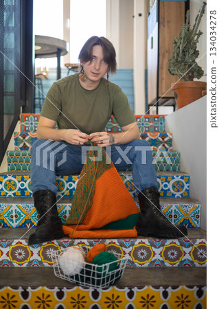 Feminine hipster man crochet handmade use hook knitting needles and wool yarn relaxing on couch 134034278