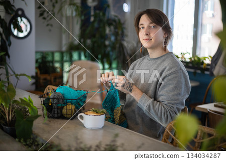 Feminine hipster man crochet handmade use hook knitting needles and wool yarn relaxing on couch Feminine hipster man crochet handmade use hook knitting needles and wool yarn relaxing on couch 134034287