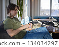 Hipster creative man crochet handmade use knitting supplies hook and wool yarn on couch at home 134034297