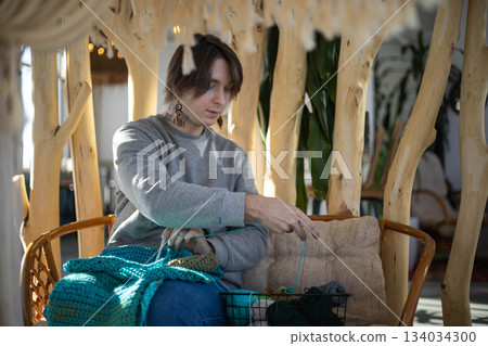 Feminine hipster man crochet handmade use hook knitting needles and wool yarn relaxing on couch 134034300