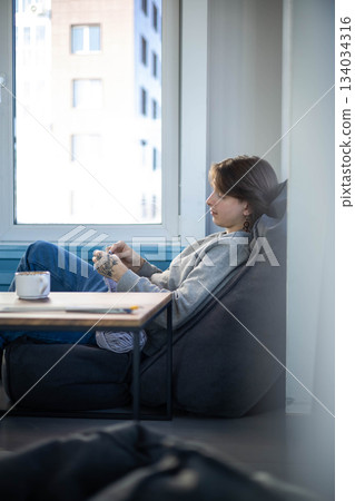 Feminine hipster man crochet handmade use hook knitting needles and wool yarn relaxing on couch 134034316