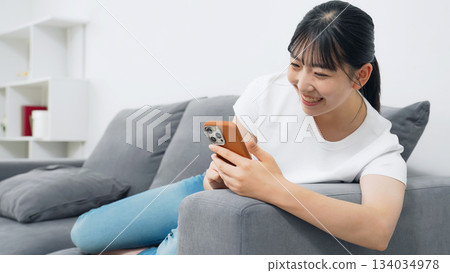 一位十幾歲的女子在客廳使用智慧型手機 一位十幾歲的女子在客廳使用智慧型手機 134034978