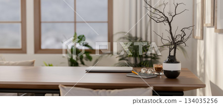 A laptop with coffee cup and glasses over book next to a vase on wooden table in living room or cafe 134035256