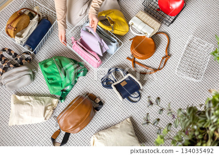 A young woman chooses fashionable, trendy, bright, multi-colored bags for herself in home wardrobe A young woman chooses fashionable, trendy, bright, multi-colored bags for herself in home wardrobe 134035492
