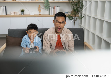 Father and son gaming together, sharing excitement and fun Father and son gaming together, sharing excitement and fun 134037040