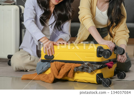 Travel Planning: Friends struggling to close an overstuffed suitcase Travel Planning: Friends struggling to close an overstuffed suitcase 134037084