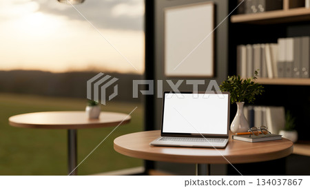 White screen laptop on wooden stool table next to bookshelf and glass wall of living room an office. White screen laptop on wooden stool table next to bookshelf and glass wall of living room an office. 134037867