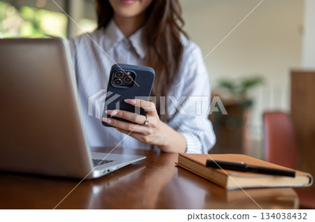 Close up of long nails woman holding and looking at phone while sitting with laptop at wooden table. Close up of long nails woman holding and looking at phone while sitting with laptop at wooden table. 134038432