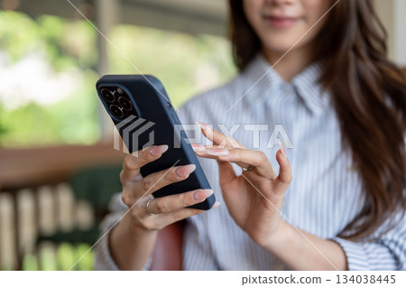 Close up of a long nails woman in blue shirt looking and typing on her phone while sitting in the cafe. Close up of a long nails woman in blue shirt looking and typing on her phone while sitting in the cafe. 134038445