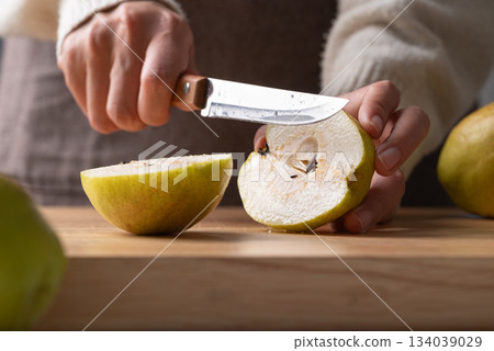 Hand holding kitchen knife and cutting pear on wooden board Hand holding kitchen knife and cutting pear on wooden board 134039029