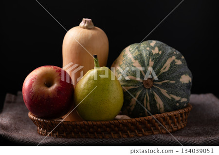 Red apple, pear and butternut squash in basket on fabric with black background 134039051