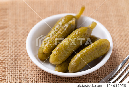 Pickled cucumber or Gherkin pickle in a bowl with fork on brown background Pickled cucumber or Gherkin pickle in a bowl with fork on brown background 134039058