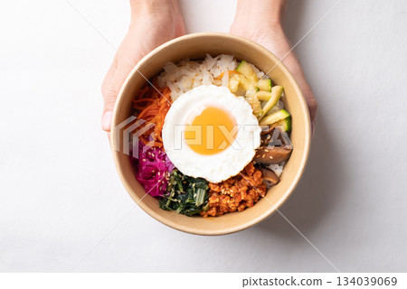 Bibimbap, Korean food, Cooked rice with vegetables, pork and egg in biodegrable bowl with hand Bibimbap, Korean food, Cooked rice with vegetables, pork and egg in biodegrable bowl with hand 134039069
