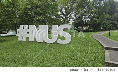 The #NUS sculpture stands beside a tree-lined slope and academic serenity in a scenic outdoor space at the National University of Singapore 134039105
