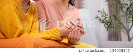 Young asian woman comforting friend with crying and depression sitting on sofa in living room. 134039595