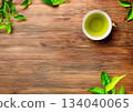 A cup of green tea and leaves on a wooden table 134040065