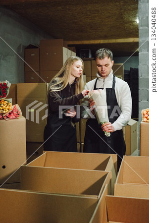 Workers organize tulip shipments carefully, Staff meticulously prepare tulips for delivery process, All workers diligently assemble and seal flower orders amidst subdued warehouse lighting Workers organize tulip shipments carefully, Staff meticulously prepare tulips for delivery process, All workers diligently assemble and seal flower orders amidst subdued warehouse lighting 134040488