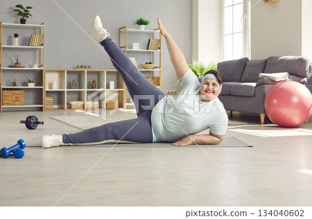 Happy overweight woman enjoying weight loss fitness workout on sports mat at home Happy overweight woman enjoying weight loss fitness workout on sports mat at home 134040602