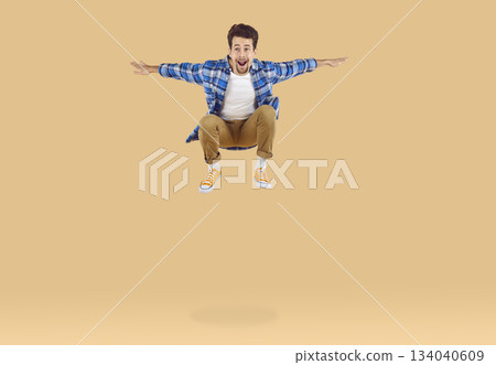 Cheerful, active and energetic young man jumping high on beige background in studio. 134040609