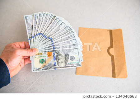 一張斜角照片顯示,左手攤開17張100美元鈔票,旁邊是一個從左側遞進來的信封。 一張斜角照片顯示,左手攤開17張100美元鈔票,旁邊是一個從左側遞進來的信封。 134040668