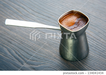 Close-up of a traditional cezve with creamy Turkish coffee on a dark wood table 134041434