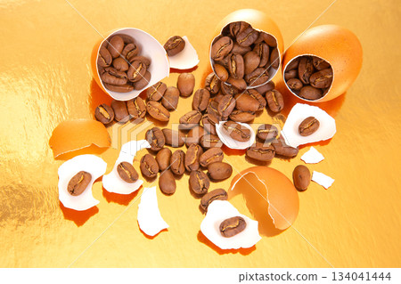 Surreal scene of coffee beans spilling from a cracked egg on a glossy gold surface Surreal scene of coffee beans spilling from a cracked egg on a glossy gold surface 134041444