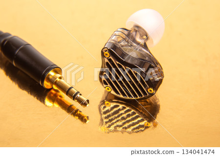earbud with a white tip, a 3.5mm audio jack, and a black audio device on a reflective gold surface 134041474