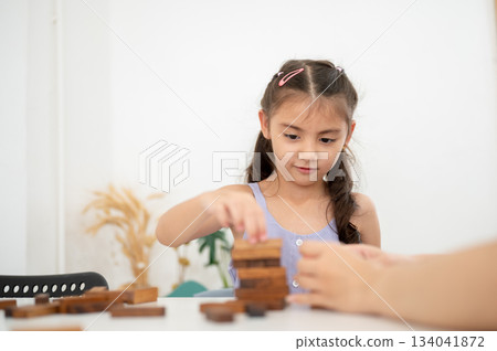 An asian kid or girl in purple shirt playing or building a wooden blocks tower on white table. 134041872