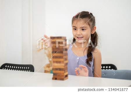 Asian kid or a little girl in purple shirt smiling while building a wooden tower on white table. Asian kid or a little girl in purple shirt smiling while building a wooden tower on white table. 134041877