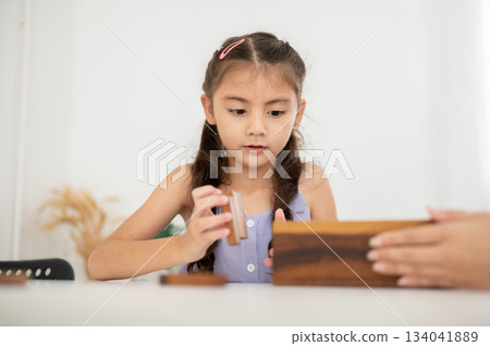 Asian kid or little girl in purple shirt is keeping wooden blocks in a box after done playing. 134041889
