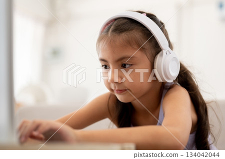 Close up of asian kid or girl wearing white headphones looking at her laptop while sitting on sofa. 134042044