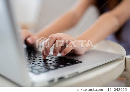Close up of a pair of kid hands typing on laptop on white table while sitting on sofa. Close up of a pair of kid hands typing on laptop on white table while sitting on sofa. 134042053