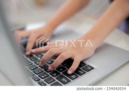 Close up of a pair of kid hands typing on laptop at white table while sitting on sofa. Close up of a pair of kid hands typing on laptop at white table while sitting on sofa. 134042054