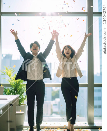 Positive business team of young men and women celebrating their success in a bright office, smiling and raising their hands in celebration of their achievement 134042764