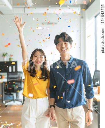 Cheerful positive business team atmosphere in the office with young men and women smiling among confetti, celebrating success and achievement 134042765