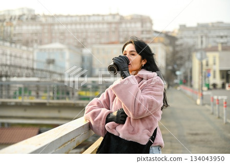 A Russian woman 50 years old drinks warm coffee from a thermo cup on a quiet city bridge in spring light enjoying calm reflection mindful energy and gentle freedom A Russian woman 50 years old drinks warm coffee from a thermo cup on a quiet city bridge in spring light enjoying calm reflection mindful energy and gentle freedom 134043950