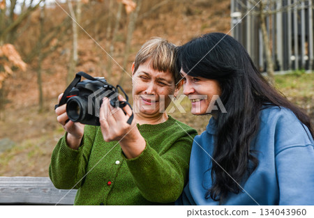 Two Russian women in their 50 years old and 60 years old laugh together while enjoying photography, showing mindfulness, freedom, active aging and creative joy. Two Russian women in their 50 years old and 60 years old laugh together while enjoying photography, showing mindfulness, freedom, active aging and creative joy. 134043960