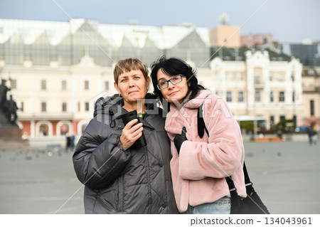 Two Russian friends, 50 and 60 years old, standing close in the city, sharing a calm moment of connection, warmth, mindfulness, and genuine female friendship. 134043961