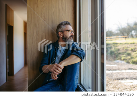 Middle aged man sitting by window and thinking. Middle aged man sitting by window and thinking. 134044150