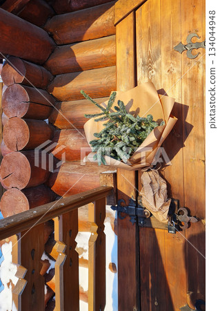 Rustic fir tree branches wrapped in kraft paper and hanging on wooden cabin wall, decorated for the winter season.  134044948