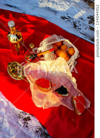 Outdoor winter picnic setup with bread, red and black caviar, oranges, and gold bottle on snow and red cloth. High quality photo Outdoor winter picnic setup with bread, red and black caviar, oranges, and gold bottle on snow and red cloth. High quality photo 134044952